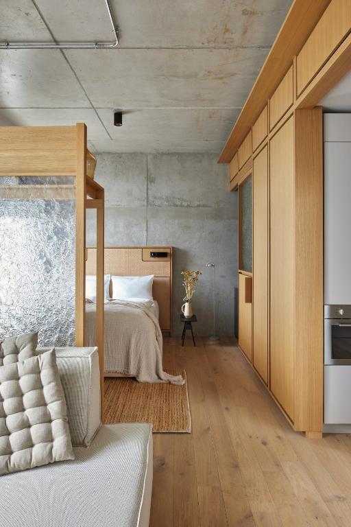 Boutique Hotels in Berlin Kreuzberg 32 Minimalist bedroom with wood accents, a bed with neutral bedding, and a textured glass dividerāreminiscent of boutique hotels in Berlin Kreuzberg. Features include built-in cabinetry, concrete walls, light wood floors, and a decorative vase with flowers.