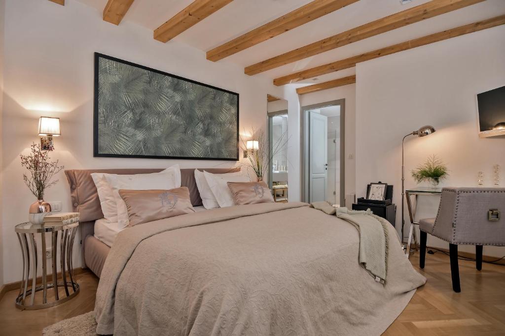 8 TOP Boutique Hotels in Split 32 A cozy bedroom reminiscent of boutique hotels in Split, featuring a large bed with beige bedding, side tables with lamps, wooden ceiling beams, a desk and chair, and modern decor illuminated by soft lighting.