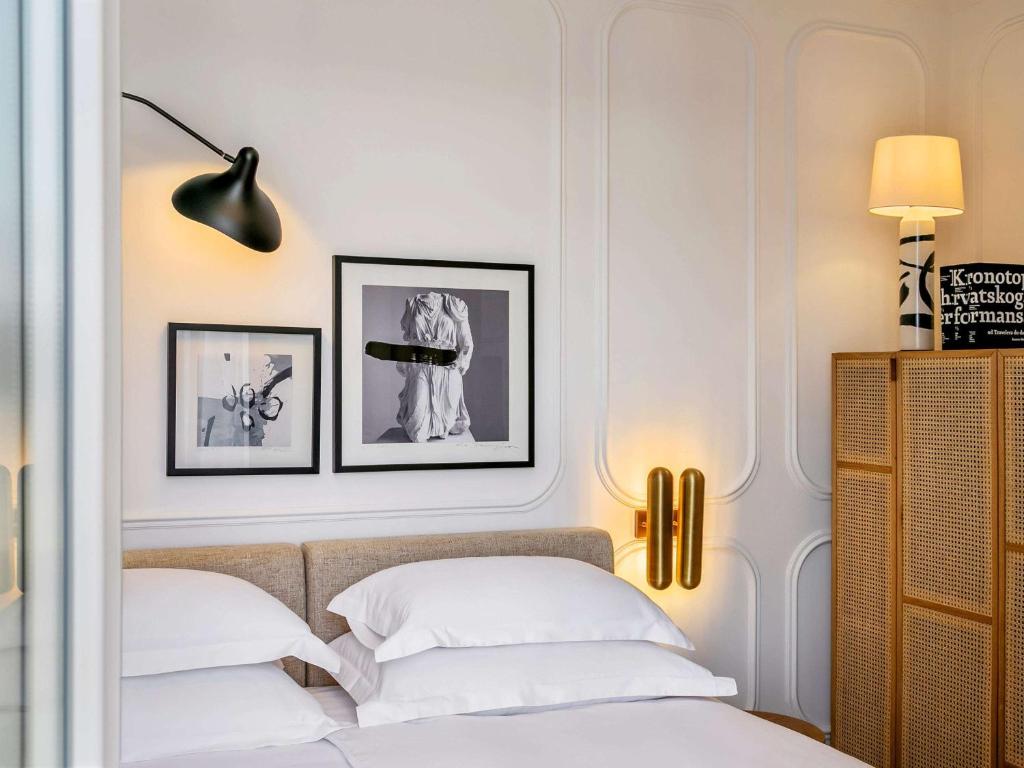 8 TOP Boutique Hotels in Split 8 A cozy, modern bedroom—ideal for those searching Where to Stay in Split—features a double bed with white bedding, black-and-white artworks above the headboard, a sleek wall lamp, floor lamp, and a wicker screen cabinet in the corner.