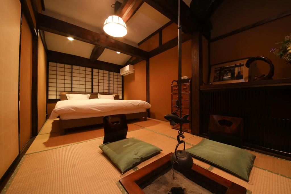 Looking for the Best Ryokan in Takayama? 2 A cozy Japanese-style room at the Best Ryokan in Takayama features tatami mats, a low table with cushions, a suspended kettle over a hearth, and a bed beneath shoji screens. Soft lighting creates a warm, inviting atmosphere.