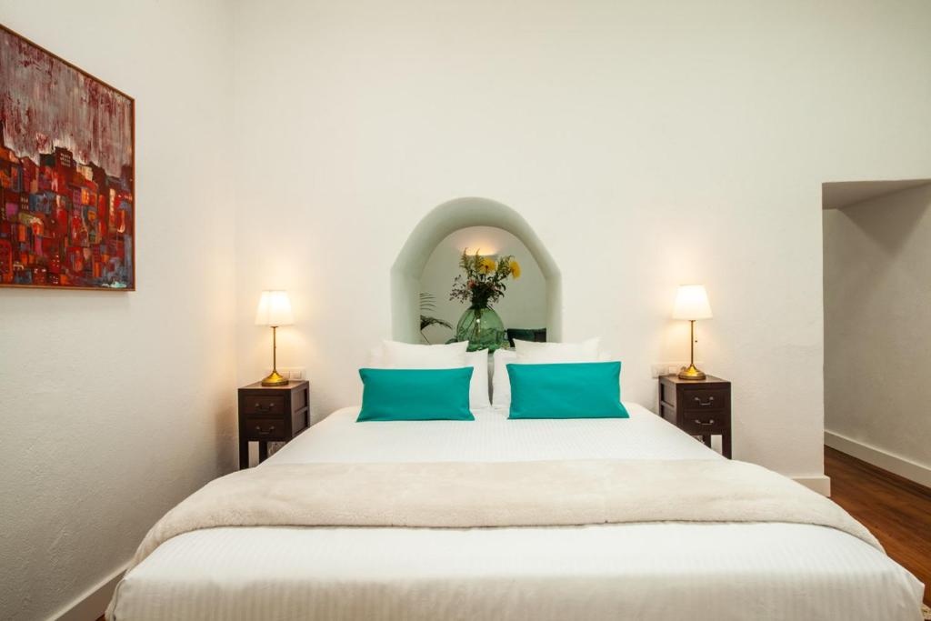 Unique Adults Only Hotels in Lanzarote 14 A neatly made bed with white linens and two teal accent pillows is centered between bedside tables with lamps. Perfect for Adults Only Hotels in Lanzarote, a vase of flowers sits above the bed, and a colorful painting hangs on the left wall.