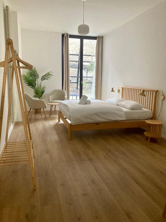 Boutique Hotels in Berlin Kreuzberg 36 This minimalist bedroom, inspired by boutique hotels in Berlin Kreuzberg, features wooden floors, a wooden bed, white bedding, two white chairs by a potted plant, a large window with curtains, and a wooden clothes rack filled with natural light.