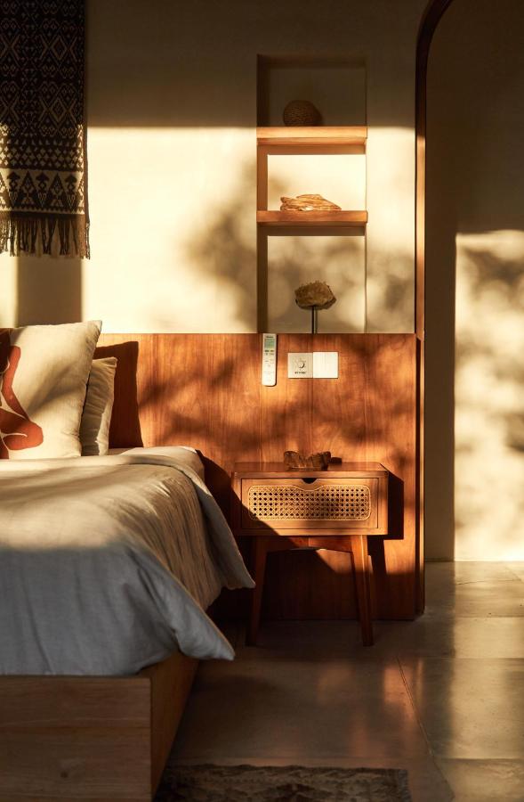 Sunlight streams into a cozy bedroom with a wooden bed, light bedding, and open shelves—just like those found in the best family villas in Bali. Warm shadows and minimal decor create a serene, inviting atmosphere.