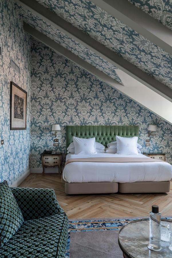 Where to Stay in Madrid: 14 Best Hotels 48 Elegant bedroom with a green tufted headboard, double bed, and vintage nightstands—perfect inspiration if you’re searching for where to stay in Madrid first time. A bottle of water sits on a round table in the foreground.