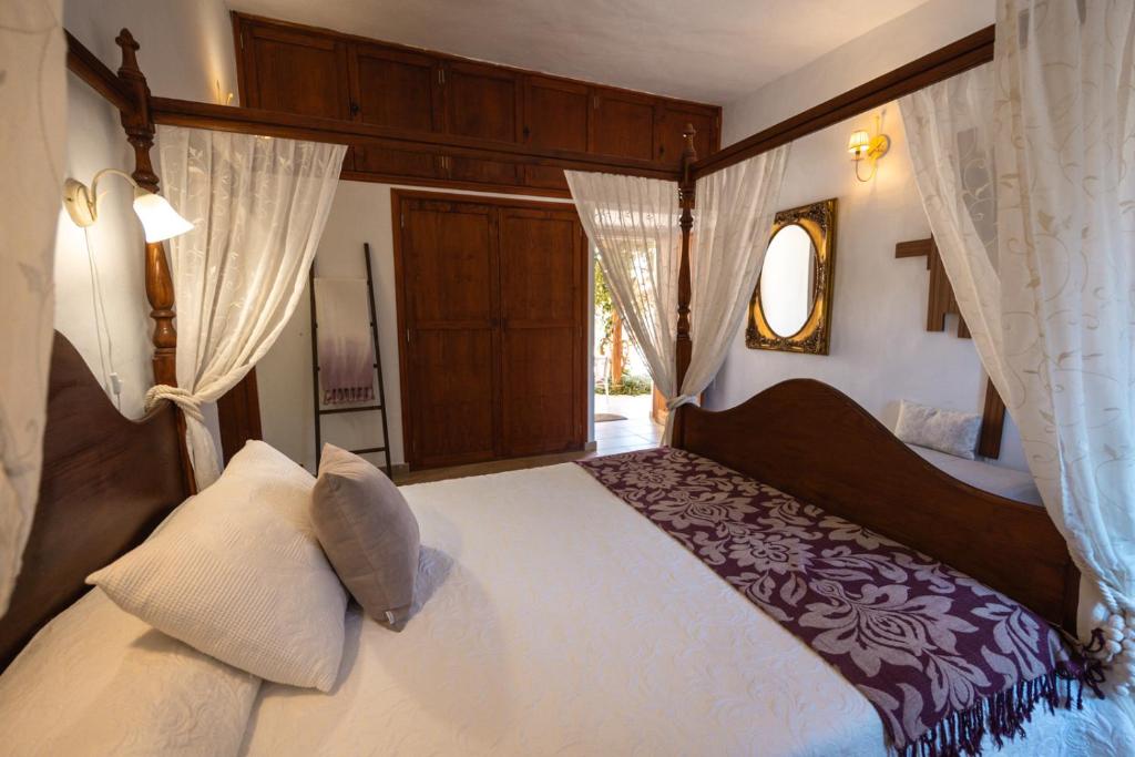 Adults Only Hotels in Fuerteventura 16 A cozy bedroom in one of the adults only hotels in Fuerteventura, featuring a wooden four-poster bed, white and beige bedding, sheer curtains, a decorative mirror, wardrobe, soft lighting, and views of greenery through an open door.