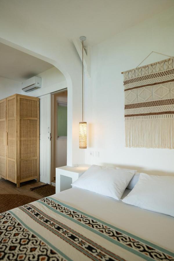 A minimalist bedroom reminiscent of the best family villas in Bali, featuring a double bed, patterned blanket, white walls, woven wall art, a rattan wardrobe, and a hanging pendant light beside the bed.