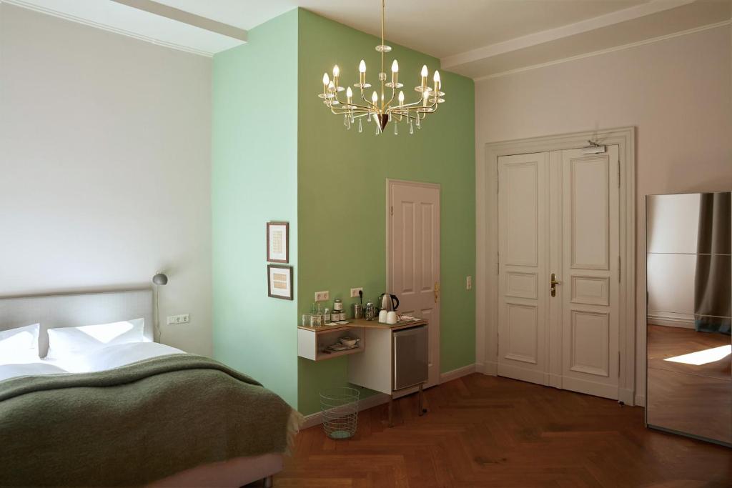Boutique Hotels in Berlin Kreuzberg 6 A bright, minimalist bedroom in the style of boutique hotels in Berlin Kreuzberg features a green accent wall, double bed, chandelier, large mirror, and a refreshment area with kettle and cups. Double doors and wooden flooring complete the modern look.