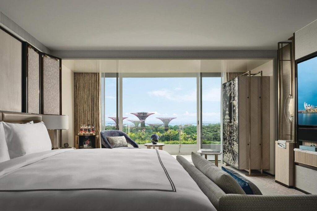 13 Most Unique Hotels in Singapore for an Incredible Holiday 4 A modern hotel room with a large bed, stylish furniture, and floor-to-ceiling windows offering a view of the Supertree Grove—an ideal choice for those seeking unique hotels in Singapore with breathtaking skyline vistas.