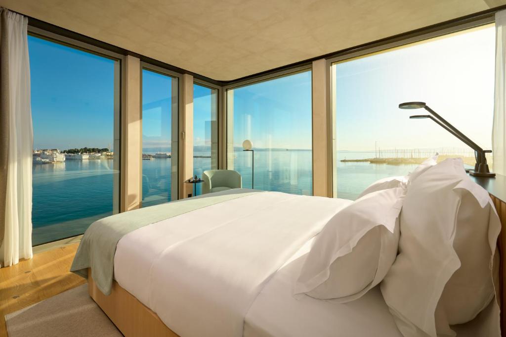 8 TOP Boutique Hotels in Split 21 A modern hotel room—perfect for those seeking Where to Stay in Split—with floor-to-ceiling windows offering a panoramic sea view. Enjoy a neatly made bed, minimalist decor, and abundant natural light.