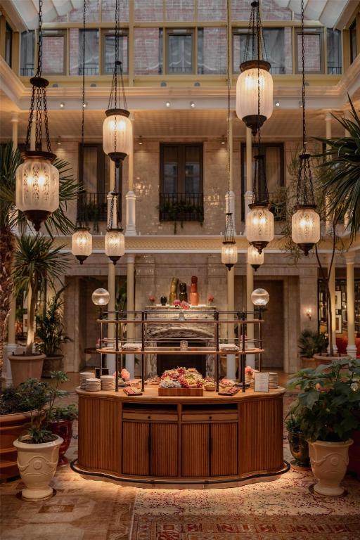 15 Best Boutique Hotels in London, UK 44 A stylish indoor atrium, inspired by boutique hotels in London, features hanging lanterns, lush potted plants, and a central wooden buffet table with food displays under glass domes amid ornate decor and large windows.