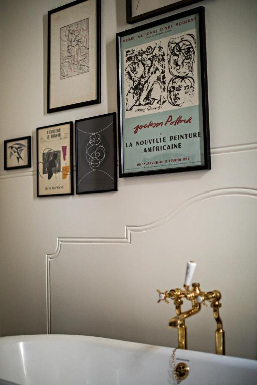 15 Best Boutique Hotels in London, UK 45 A wall above a white bathtub with gold fixtures displays several framed art prints and posters, including a French Jackson Pollock print. The gallery-style arrangement evokes the curated elegance of boutique hotels in London.