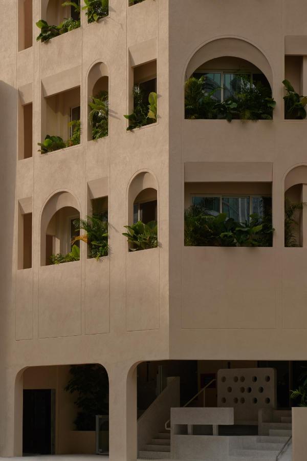 13 Most Unique Hotels in Singapore for an Incredible Holiday 37 A modern beige building with large arched windows and balconies, featuring lush greenery on each level. This minimalist design with soft shadows and clean lines stands out among unique hotels in Singapore.