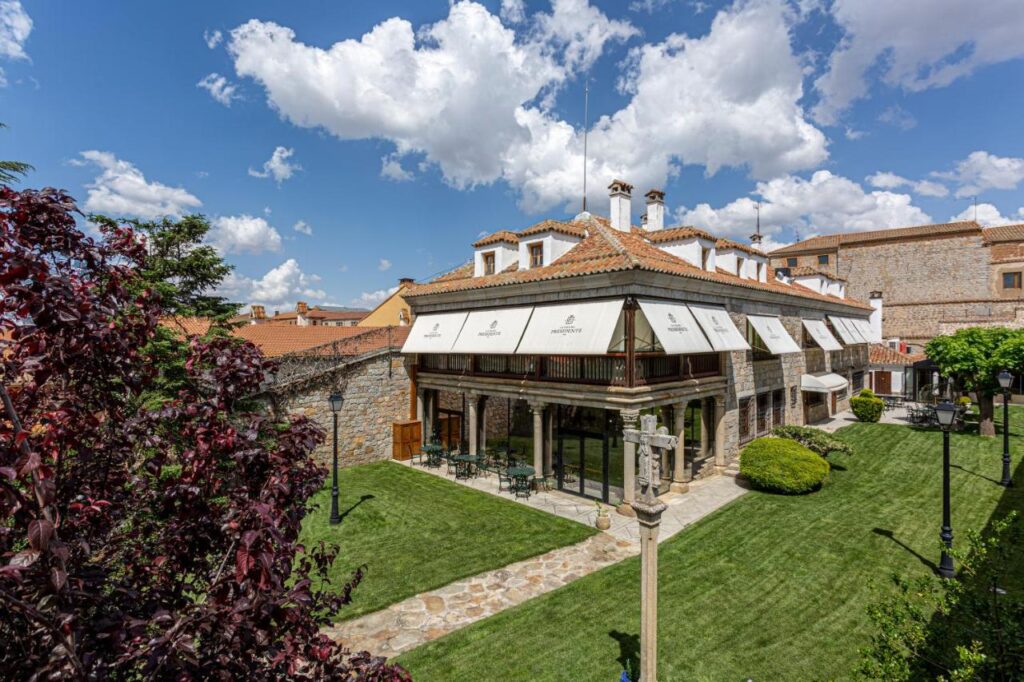 25 Weekend Trips from Madrid Max. 2h Away 101 A stone building with a red-tiled roof and large white awnings sits beside a manicured lawn under a blue sky—an idyllic spot often featured in weekend trips from Madrid, complete with trees and a welcoming stone pathway in front.
