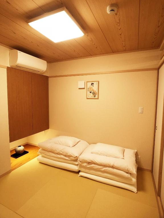 8 BEST Ryokans in Osaka 7 A minimalist Japanese-style room inspired by ryokans in Osaka, featuring tatami mats, two stacked white futon beds, wooden ceiling and cabinets, a small alcove with a teapot, and a framed picture on the wall.