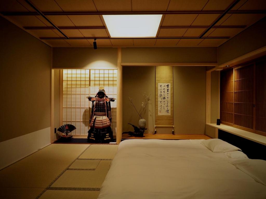 7 UNIQUE Ryokans in Gion Kyoto 5 A minimalist Japanese-style bedroom with tatami flooring, a low bed, and a suit of samurai armor displayed near shoji screens, echoing the tranquil elegance found in ryokans in Gion Kyoto. A scroll and fan enhance the serene atmosphere.