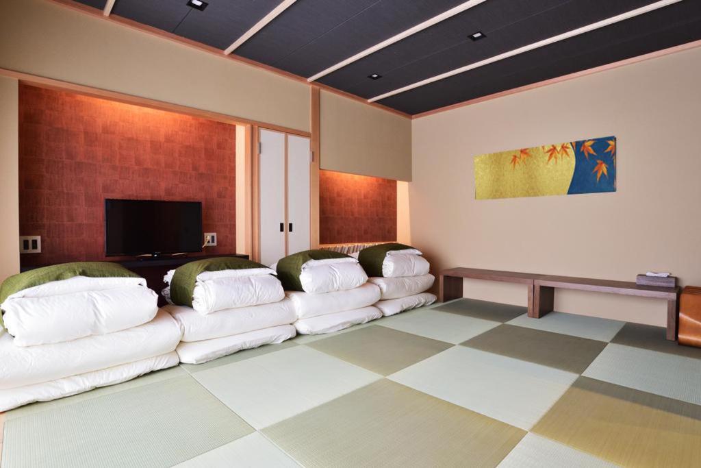 8 BEST Ryokans in Osaka 15 A Japanese-style room with tatami mats, four stacked futon beds, a low bench, a TV, and autumn leaf wall art. The minimalist design offers the serene ambiance typical of ryokans in Osaka.