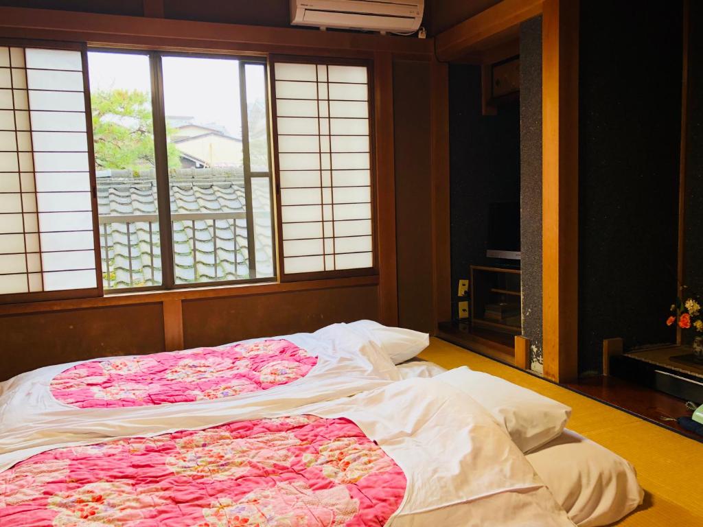 Looking for the Best Ryokan in Takayama? 19 A traditional Japanese room at the Best Ryokan in Takayama with two futons on tatami mats, pink floral quilts, and shoji doors opening to rooftop views. A small TV and flower arrangement add charm in the corner.