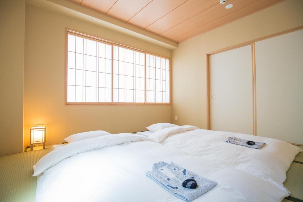 8 BEST Ryokans in Osaka 11 A minimalist Japanese-style bedroom inspired by ryokans in Osaka, with futons on a tatami mat floor, folded yukata robes and towels on top, shoji paper windows, sliding doors, and a soft glowing lantern in the corner.