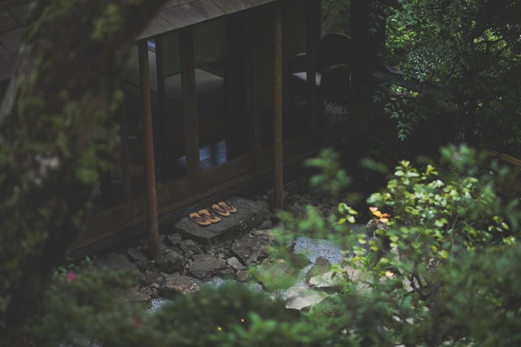 8 BEST Ryokans in Osaka 34 A pair of traditional sandals are placed neatly on a stone step outside a wooden building, surrounded by lush green trees—evoking the tranquil atmosphere found at ryokans in Osaka.