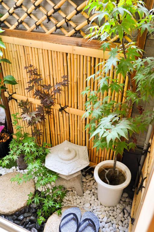 8 BEST Ryokans in Osaka 8 A small Japanese-style garden with maple plants, a white stone lantern, white pebbles, round stone steps, and striped sandals set against a bamboo fence—reminiscent of tranquil ryokans in Osaka.