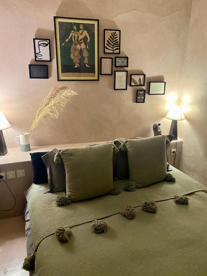12 Charming Budget Riads in Marrakech 14 A cozy bedroom inspired by budget riads in Marrakech, with a neatly made bed featuring green pillows, a tasseled blanket, two lit lamps on either side, and a gallery wall of framed art above the headboard.