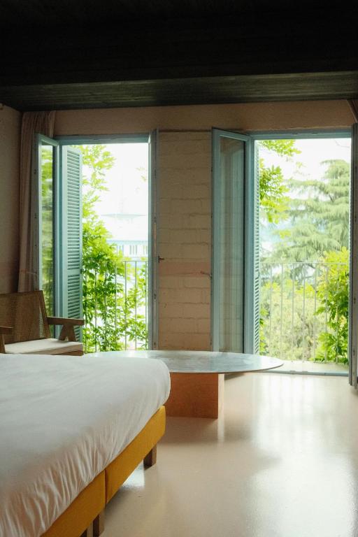11 Unique Hotels in Georgia You Can't Miss! 39 A bright bedroom with a white bed, yellow bed frame, wooden chair, and a table, featuring open double doors that overlook green trees and let in natural lightāa charming example of unique hotels in Georgia.