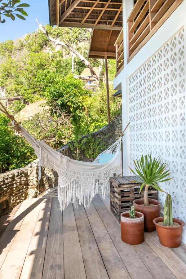 A white hammock with fringe hangs on a wooden deck beside a white patterned wall, surrounded by potted plants and lush greenery—an inviting scene reminiscent of the best family villas in Bali.