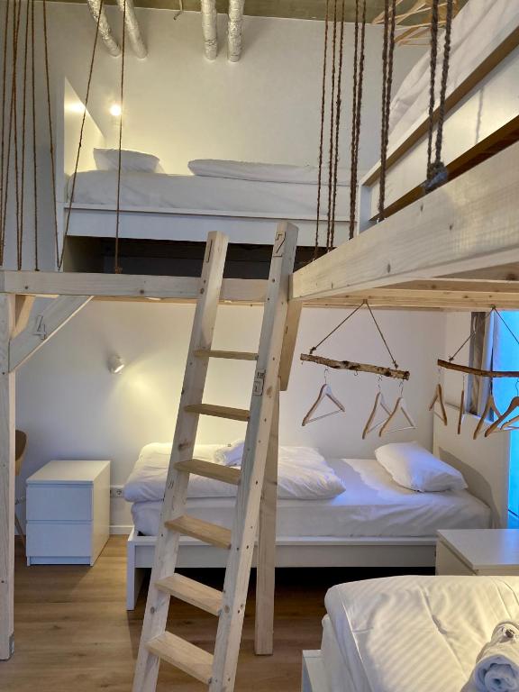 Boutique Hotels in Berlin Kreuzberg 39 A modern hostel-style room, inspired by boutique hotels in Berlin Kreuzberg, with two wooden loft beds accessed by ladder, two single beds below, white bedding, nightstands, and hanging clothes racks with wooden hangers.