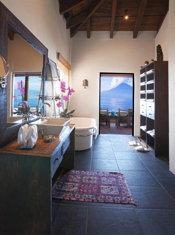 8 UNIQUE Places Where to Stay in Lake Atitlán 16 A modern bathroom with a wooden vanity, bathtub, and open shelves, featuring large slate tiles and a patterned rug—an inviting retreat for those seeking where to stay in Lake Atitlan with lake and mountain views from the patio.