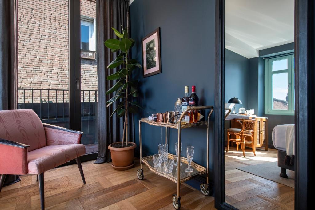 11 Unique Hotels in Georgia You Can't Miss! 28 A cozy room in one of the unique hotels in Georgia, with blue walls, a pink armchair, a tall potted plant, a bar cart with drinks and glasses, and sunlit views into a bedroom with a desk and bed. Large windows fill the space with natural light.