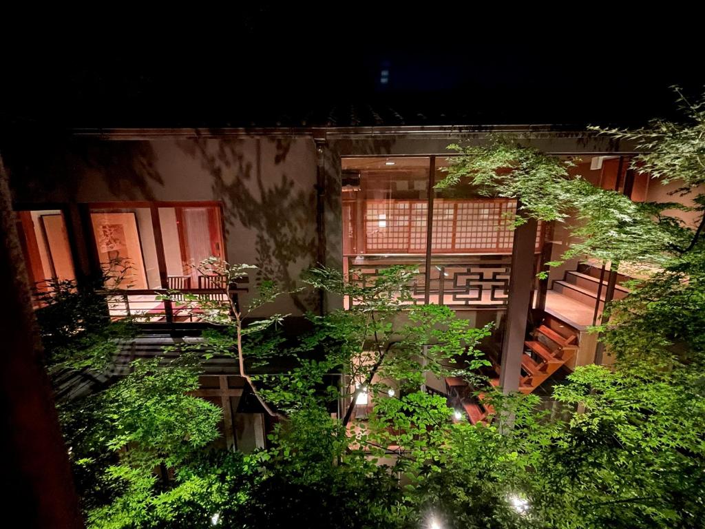 7 UNIQUE Ryokans in Gion Kyoto 19 A warmly lit traditional building with large windows and wooden details, much like the ryokans in Gion Kyoto, is surrounded by lush green trees at night, creating a serene and inviting atmosphere.