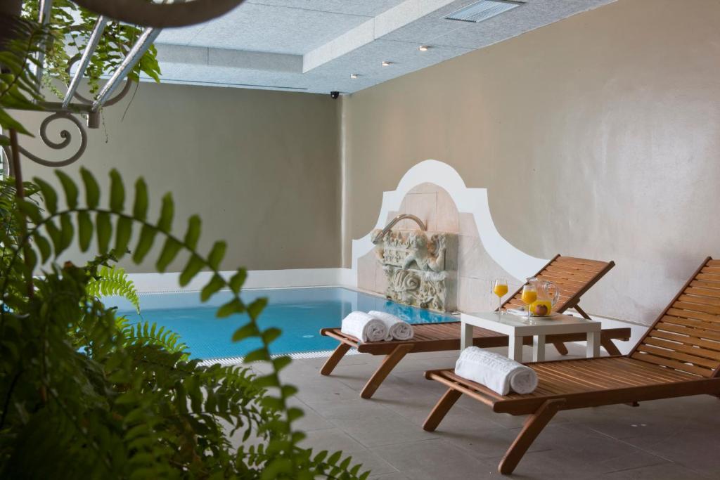 8 Unique Boutique Hotels in Bilbao Spain 21 Two wooden lounge chairs with rolled white towels face an indoor pool with a decorative water feature—a scene often found in boutique hotels in Bilbao. A small table holds drinks and snacks, while green ferns add to the calm, relaxing setting.