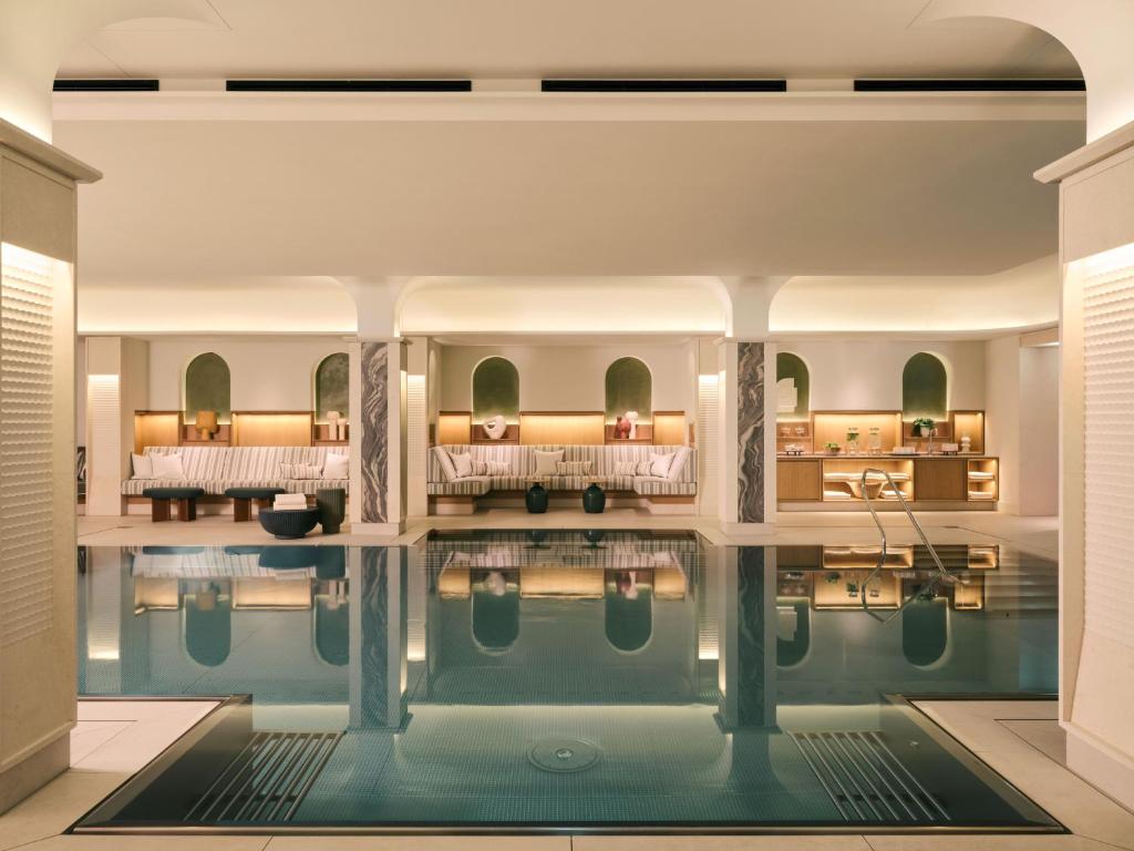 Authentic Boutique Hotels in Munich 30 Indoor luxury swimming pool with calm water, surrounded by elegant lounge seating, soft lighting, and modern decor—just what you’d expect from the finest boutique hotels in Munich. The serene atmosphere is enhanced by the tranquil reflections on the pool’s surface.