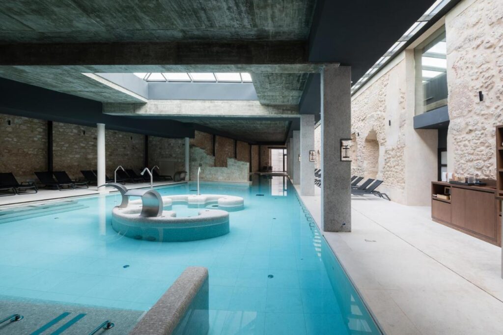 25 Weekend Trips from Madrid Max. 2h Away 97 Indoor pool area with modern concrete and stone walls, lounge chairs along the sides, and a circular water feature. Perfect for relaxing weekend trips from Madrid, skylights above fill the spacious, minimalist setting with natural light.