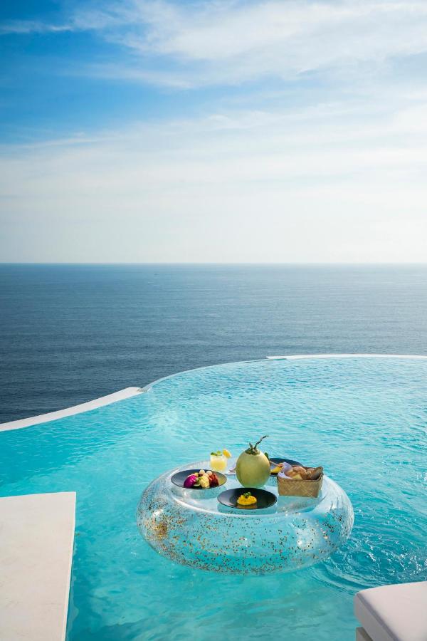 A floating tray with snacks, fruit, and a coconut drink sits on an infinity pool at one of the best family villas in Bali, overlooking a calm, expansive ocean under a partly cloudy sky.