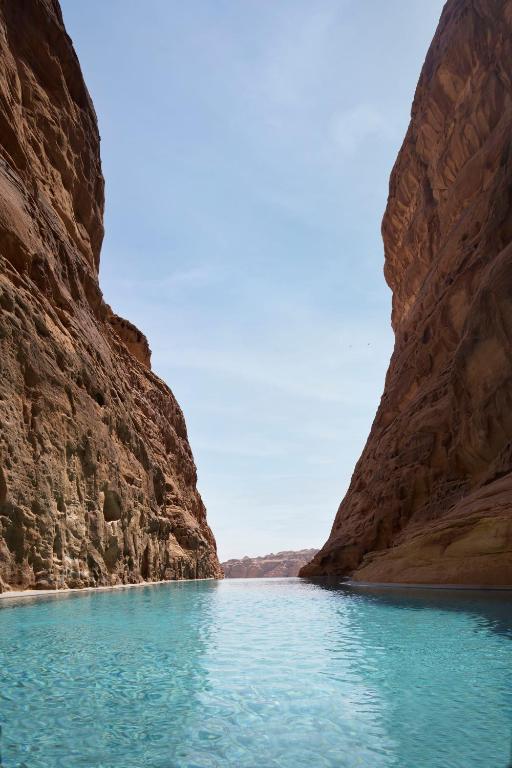 9 Best Hotels in Saudi Arabia: Unique Stays Across the Country 14 Clear blue water flows between two towering, rugged rock cliffs under a bright sky, creating a serene canyon landscape—an experience to complement a stay at the Best Hotels in Saudi Arabia.