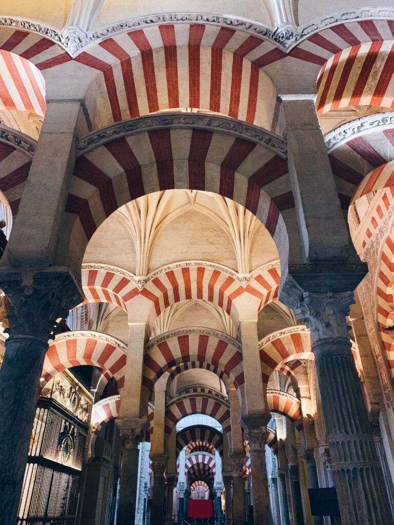 Rows of stone arches with alternating red and white stripes, supported by columns, fill this historic, ornately designed building with vaulted ceilings—a must-see if visiting Cordoba one day.