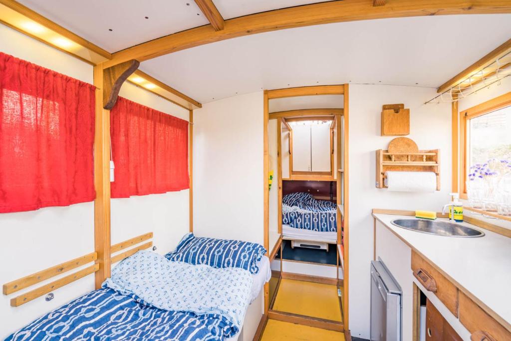 Boutique Hotels in Berlin Kreuzberg 41 A cozy camper interior with wooden accents evokes the charm of boutique hotels in Berlin Kreuzberg, featuring two beds with blue patterned bedding, red curtains, a petite kitchenette, and shelves bathed in bright natural light.