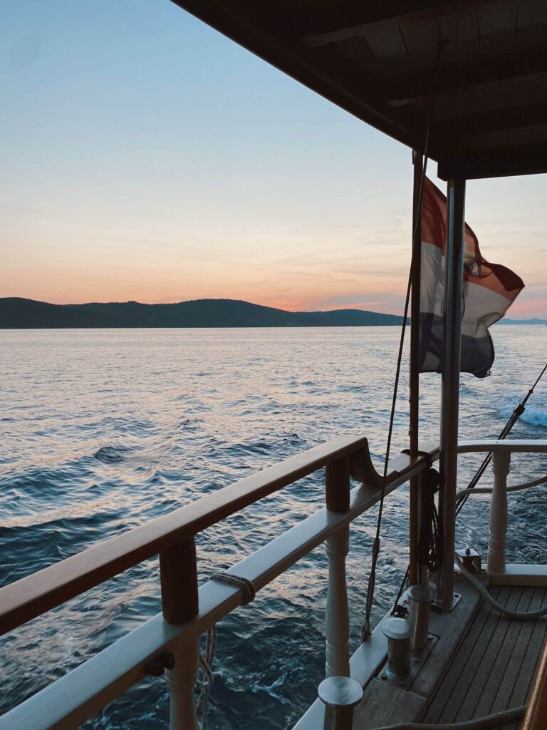 8 TOP Boutique Hotels in Split 37 A view from a boat at sunset near Split, with calm ocean waters, distant hills on the horizon, and a red, white, and blue striped flag—perfect inspiration for planning where to stay in Split.
