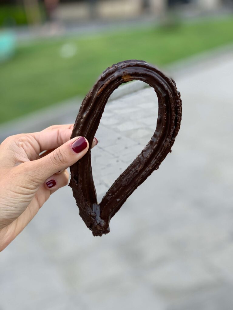 1 day in Seville Spain: My Favorite City 13 A hand with dark red nail polish holds a clear teardrop-shaped piece of glass, its edge coated in chocolate, against a blurred outdoor background—capturing a sweet moment reminiscent of 1 day in Seville, Spain.