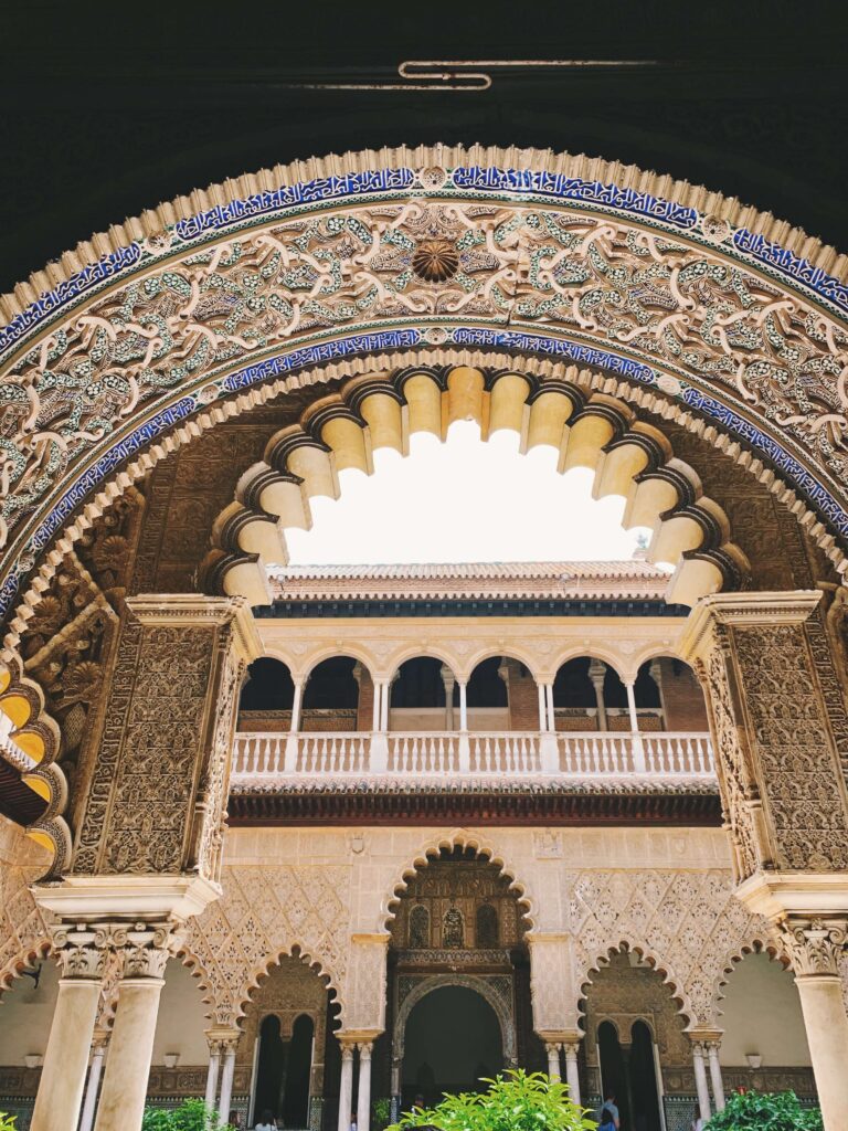 1 day in Seville Spain: My Favorite City 14 An ornate horseshoe arch with intricate Islamic patterns frames a courtyard of a historic palace in Seville, perfect for discovering during 1 day in Seville Spain—detailed carvings and columns glow under bright daylight.