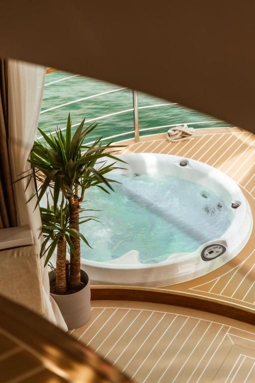 Where to Stay in Split: Hotel & Areas Guide 34 A round outdoor hot tub with bubbling water sits on a wooden deck beside a potted plant, overlooking a body of green water—a serene spot that hints at why it's a top pick for those seeking where to stay in Split. Part of a white curtain and railing frame the scene.