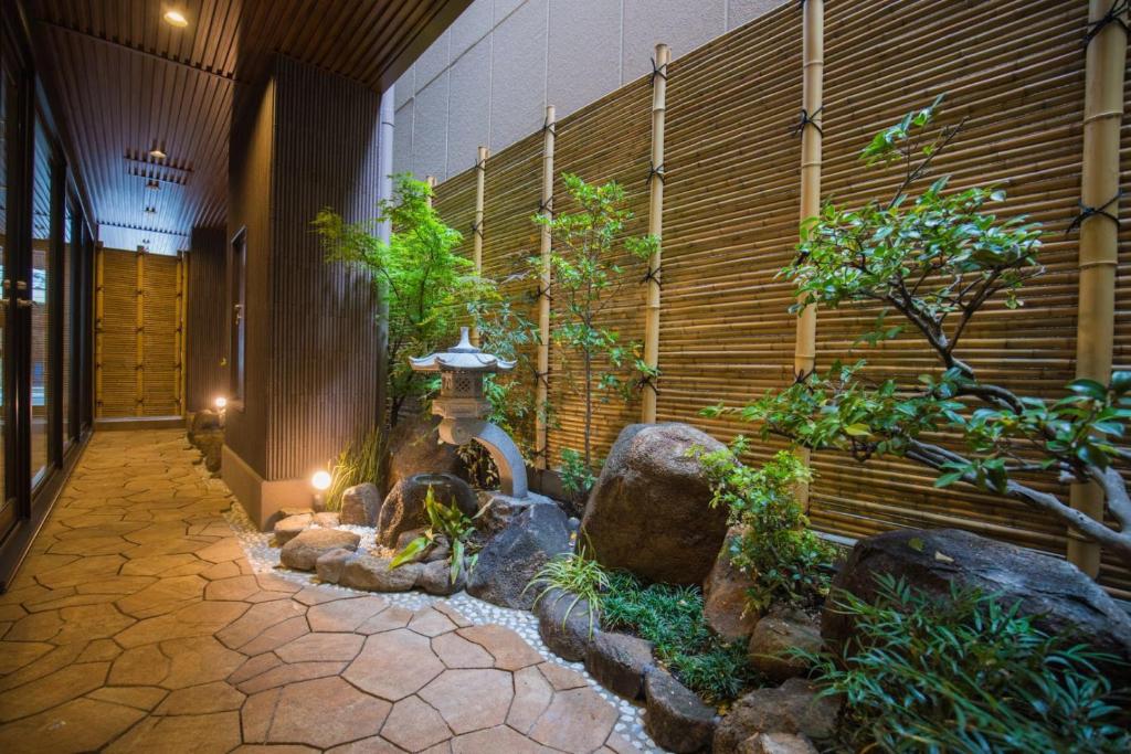 8 BEST Ryokans in Osaka 14 A narrow stone pathway runs beside a traditional Japanese garden at one of the ryokans in Osaka, with bamboo fencing, green plants, rocks, and a stone lantern softly lit by small ground lights.
