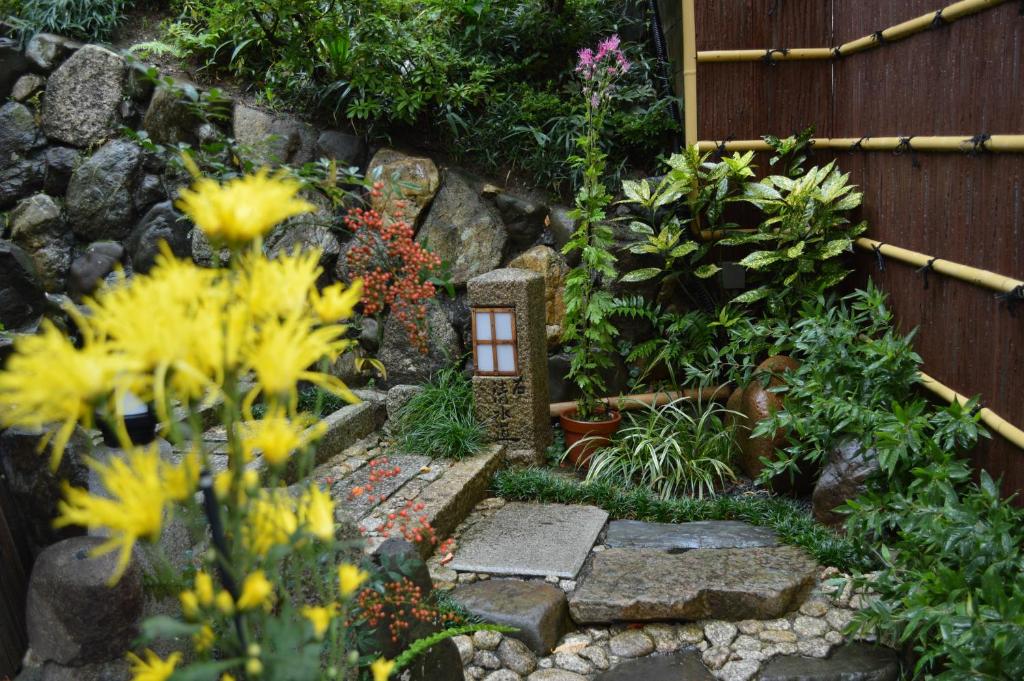 7 UNIQUE Ryokans in Gion Kyoto 18 Stone steps lead through a lush Japanese garden with yellow flowers, green plants, a stone lantern, and a bamboo fence along the right—reminiscent of tranquil ryokans in Gion Kyoto. Mossy rocks form the backdrop.