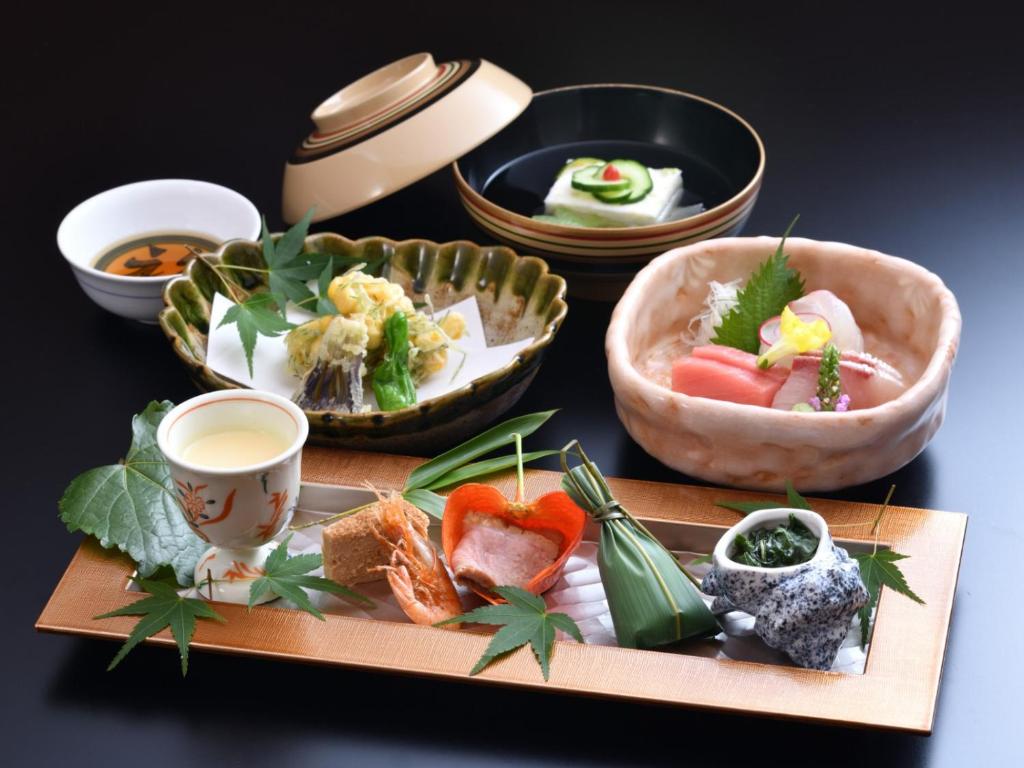 7 UNIQUE Ryokans in Gion Kyoto 25 A beautifully arranged Japanese kaiseki meal, like those served at ryokans in Gion Kyoto, featuring assorted sashimi, tempura, tofu, soup, and various appetizers, all elegantly presented on decorative dishes with garnishes and maple leaves.