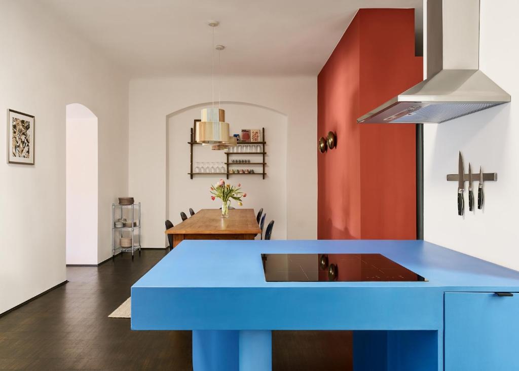 Boutique Hotels in Berlin Kreuzberg 21 Modern kitchen with a bold blue island, built-in black stovetop, and stainless steel range hoodāreminiscent of the chic interiors found in boutique hotels in Berlin Kreuzberg. A wooden dining table sits by a red accent wall, surrounded by shelves and kitchenware.