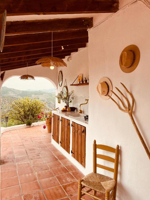Adults-Only Hotels in Costa del Sol 33 A rustic outdoor kitchen with white stucco walls, wooden cabinets, a yellow chair, and hats hanging on the wall—perfect for guests of adult only hotels in Costa del Sol—overlooking green hills and a cloudy sky in the background.