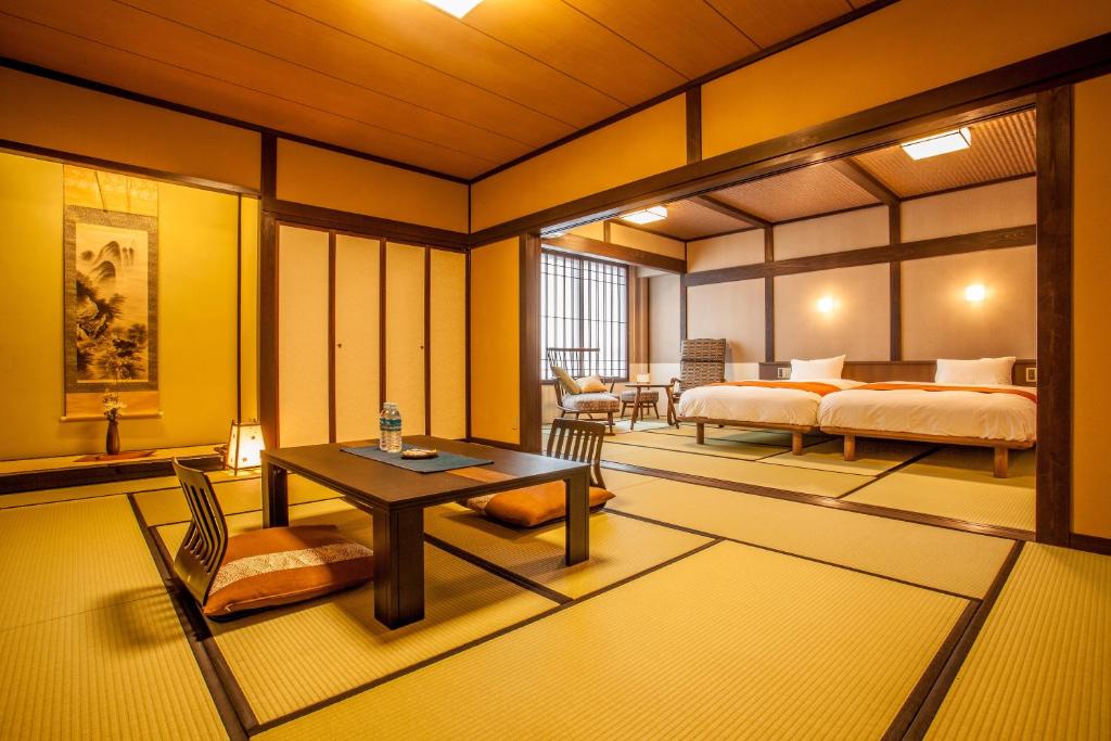 Looking for the Best Ryokan in Takayama? 11 A spacious traditional Japanese tatami room at one of the Best Ryokan in Takayama, featuring a low table with floor chairs and two beds beside a large window with shoji screens. Warm lighting creates a cozy atmosphere.
