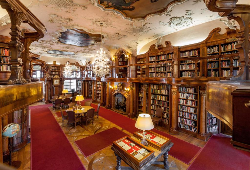 Unique Boutique Hotels in Salzburg 14 An ornate, historic library with wooden bookshelves, red carpets, chandeliers, and a decorated ceiling—reminiscent of the refined ambiance found in boutique hotels in Salzburg—creates an elegant and inviting atmosphere for reading.