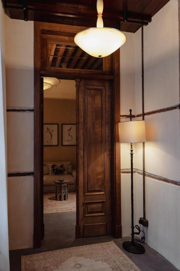 9 Best Hotels in Saudi Arabia: Unique Stays Across the Country 3 A cozy hallway inspired by the elegant interiors of the best hotels in Saudi Arabia, with a wooden door, beige rug, and floor lamp. The warmly lit living room beyond features wood accents, neutral tones, and tasteful framed artwork.